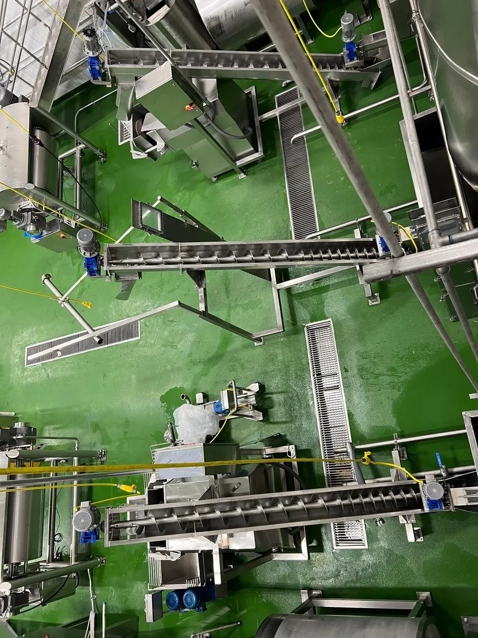 Overhead view of a food plant line layout: screw conveyors, drains and stainless equipment